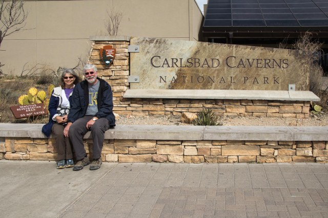 Two people sitting near Carlsbad Caverns National Park sign