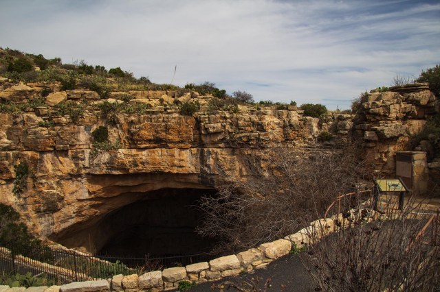 Wispy clouds, blue sky, rock cliffs and cave entrance