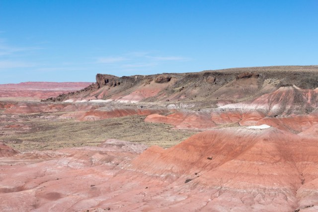 Green plateau with pink and red cliffs under blue sky