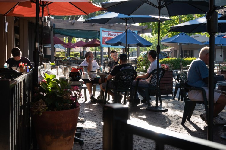 People sitting under blue and red umbrellas at tables