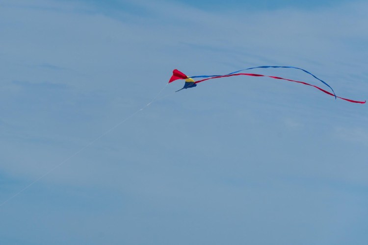 Red, yellow, and blue kite with red and blue streamers against the sky