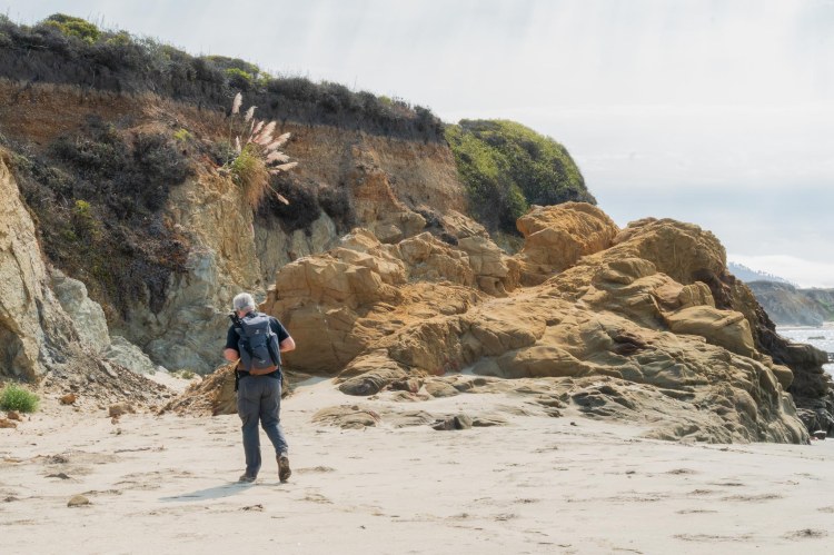 Man with backpack walking near an ocean cliff