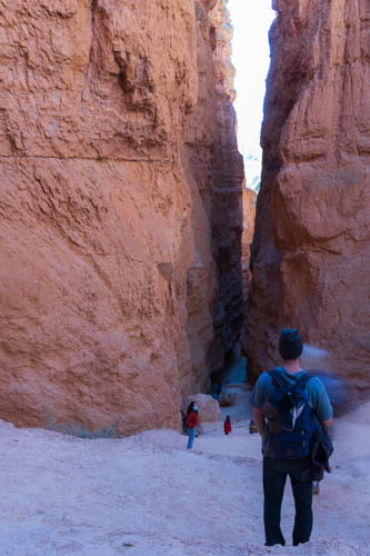 Hiker standing in front of a tall narrow slot between rock cliffs