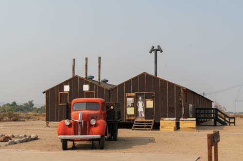 World War II era red delivery pick up with wood framed tar papered brown buildings in background