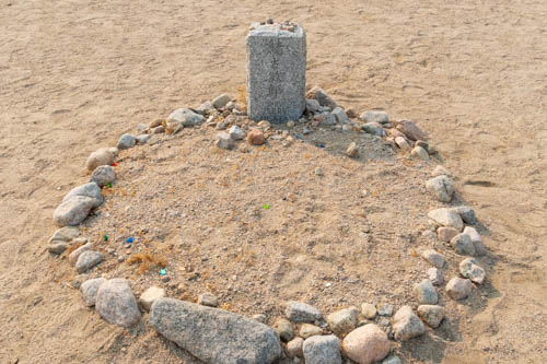 Round gravesite outlined with rocks in the sand and headstone