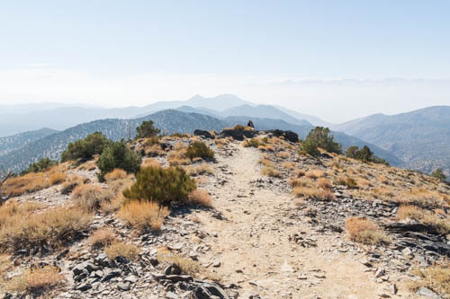 Landscape view of trail, shrubs, mountains, and smokey skies