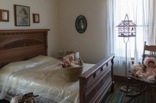 Bedroom inside early 1900s house with bird cage, wood carved bed, rocking chair, and dolls