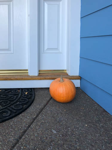 Pumpkin on doorstep of blue house with white trim