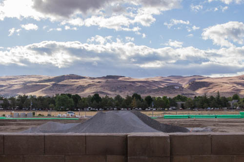 Fluffy clouds over brown hills, line of trees, gravel mound, and brick wall