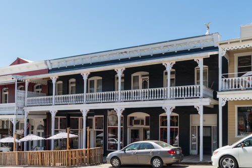 Dark green two story 1800s building with white railings on top floor