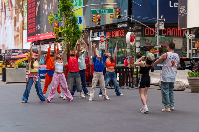 A group of dancers performing in a busy New York City street, wearing colorful outfits and showcasing energetic moves in Times Square.