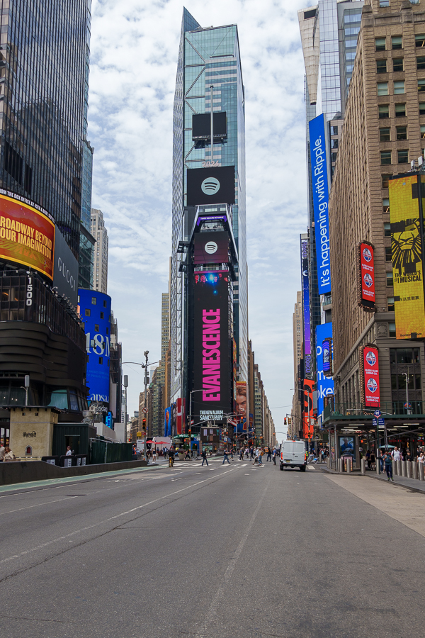 View of Times Square in New York City, featuring tall skyscrapers with bright digital billboards and a mostly empty street, under a cloudy sky.