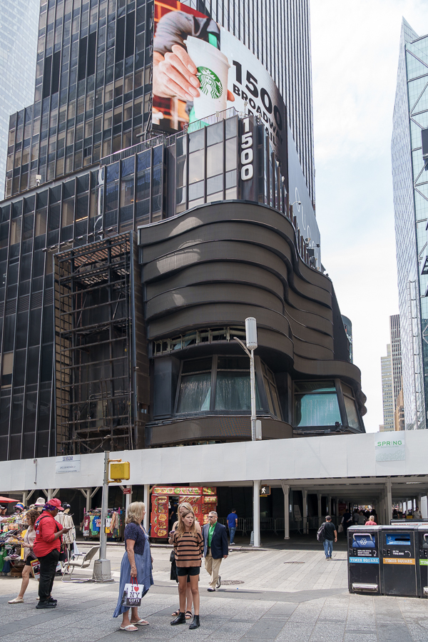 View of a modern building at 1500 Broadway in Times Square, featuring a large Starbucks advertisement and people walking on the street.