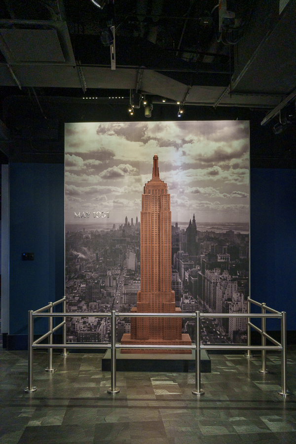 A model of the Empire State Building on display in front of a historic photograph of New York City, with a date inscription of May 1931.