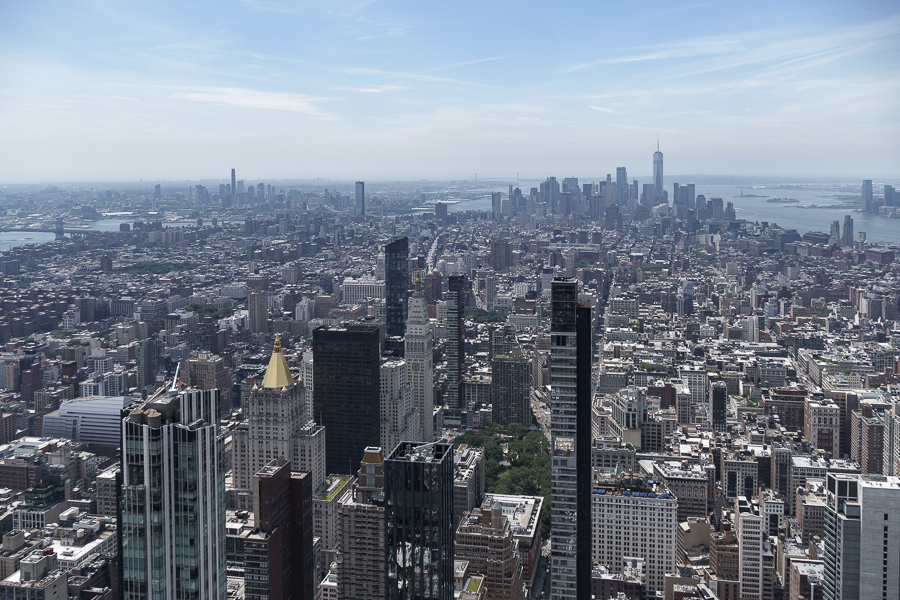 A panoramic view of a bustling city skyline, showcasing a mix of modern skyscrapers and architectural landmarks with a river and distant skyline in the background.