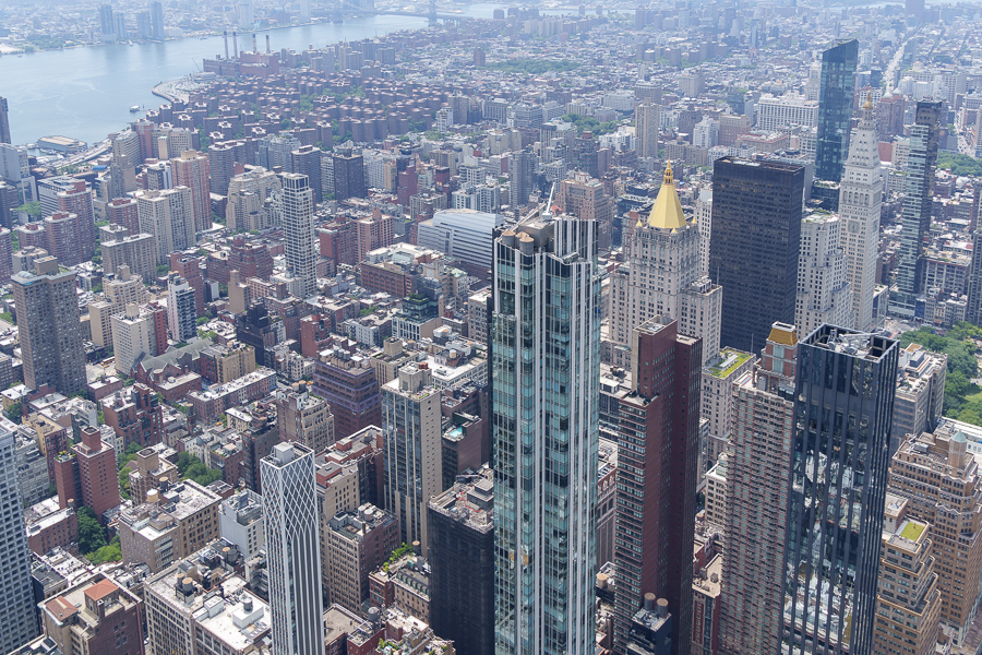 Aerial view of a densely populated urban area with various skyscrapers, including modern glass buildings and historic structures, overlooking a river in the background.