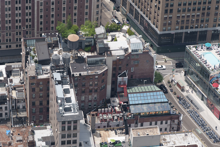 Aerial view of a cityscape featuring a mix of brick and modern buildings, with visible rooftops, greenery, and urban infrastructure.