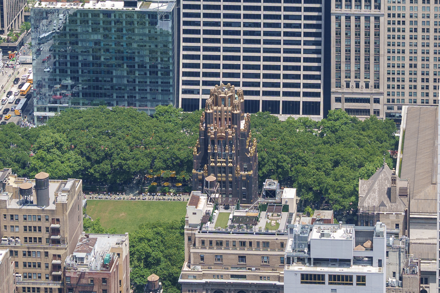 Aerial view of a prominent art deco skyscraper surrounded by lush greenery, with modern buildings in the background.