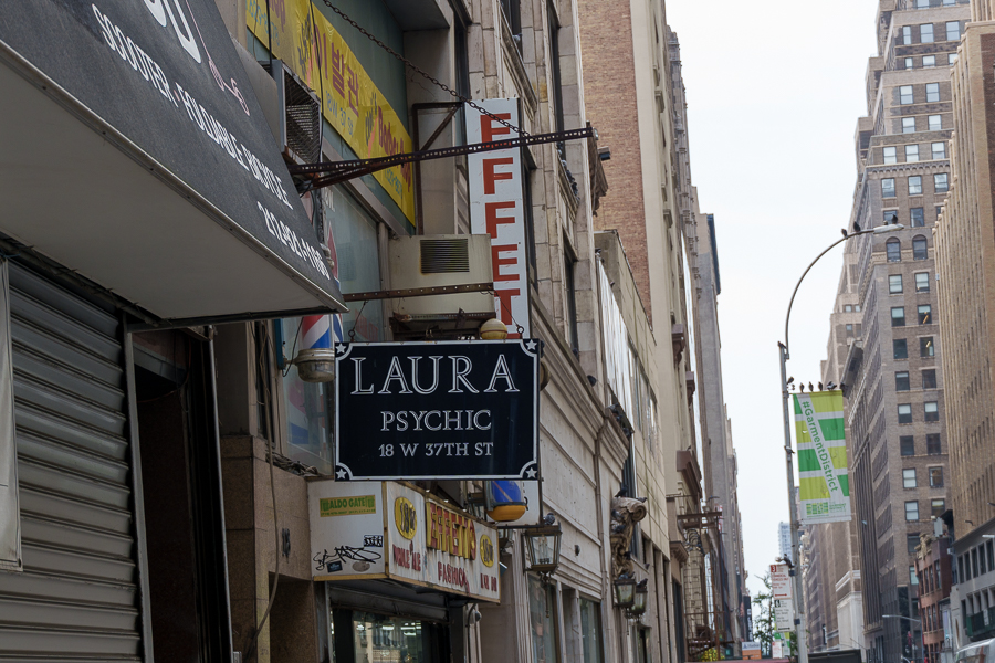 Street view featuring a sign for 'Laura Psychic' on W 37th St, surrounded by storefronts and buildings.
